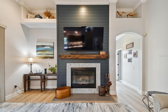 living area with baseboards, wood finished floors, a fireplace, and crown molding