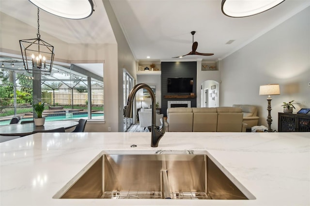 kitchen with light stone counters, a ceiling fan, a fireplace, a sink, and pendant lighting