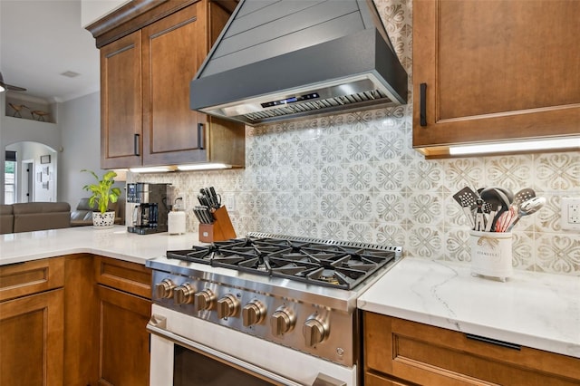 kitchen featuring arched walkways, tasteful backsplash, stainless steel range with gas cooktop, and wall chimney range hood