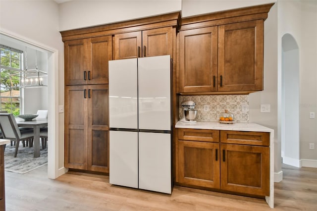 kitchen featuring brown cabinetry, arched walkways, freestanding refrigerator, decorative backsplash, and light countertops