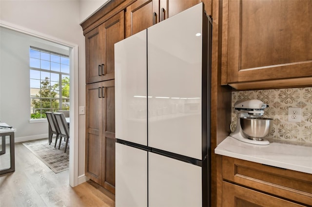 kitchen featuring light wood-style flooring, brown cabinets, freestanding refrigerator, and baseboards