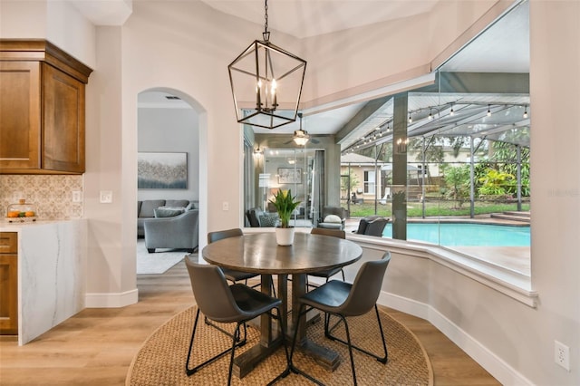 dining room with arched walkways, baseboards, and light wood finished floors