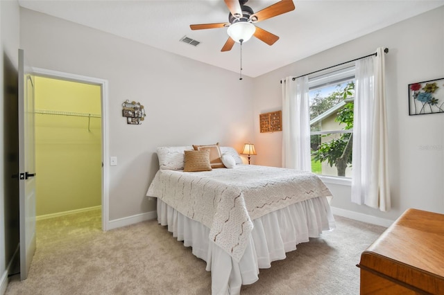 bedroom with visible vents, baseboards, light colored carpet, and a walk in closet