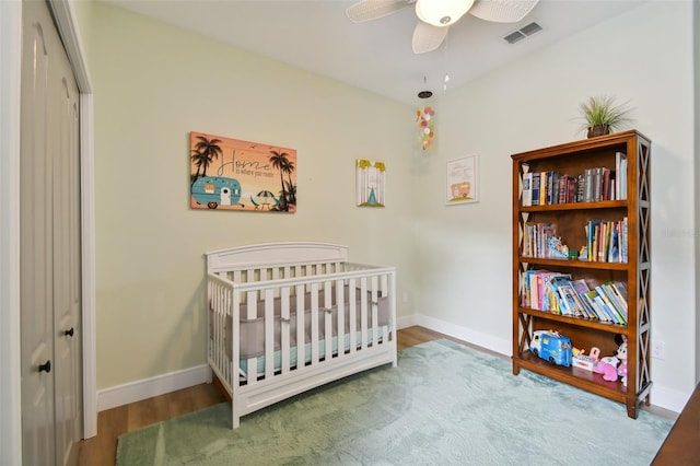 bedroom with visible vents, baseboards, wood finished floors, a closet, and a nursery area