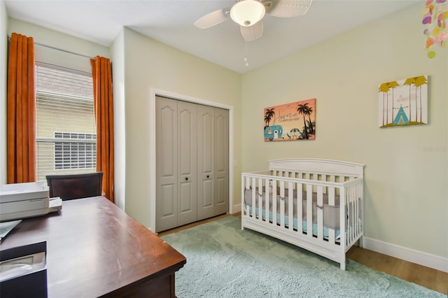 bedroom with a crib, a ceiling fan, wood finished floors, a closet, and baseboards