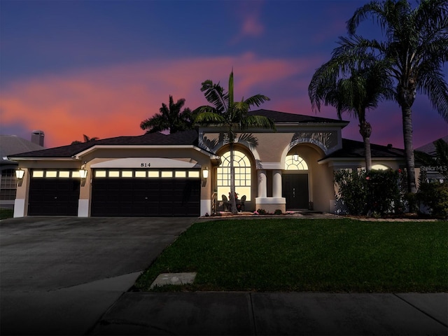 mediterranean / spanish-style house with an attached garage, a yard, driveway, and stucco siding