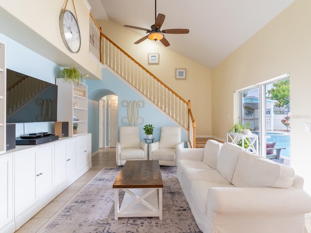 living area with high vaulted ceiling, a ceiling fan, arched walkways, light tile patterned floors, and stairs