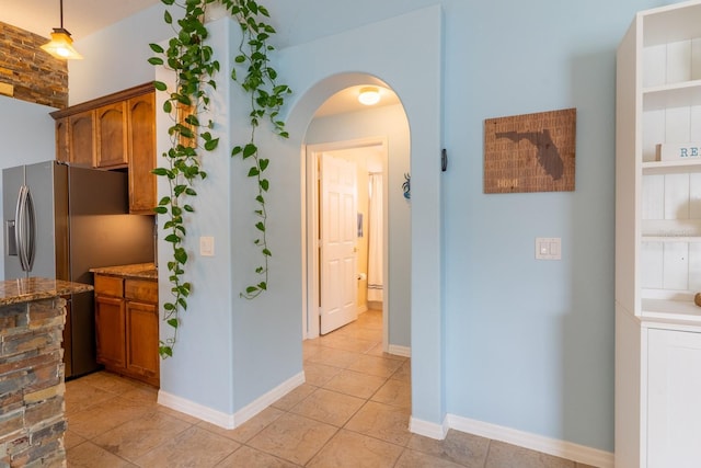 kitchen featuring dark stone countertops, baseboards, stainless steel fridge with ice dispenser, arched walkways, and brown cabinets