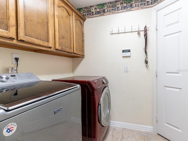 laundry room featuring washing machine and clothes dryer, cabinet space, a textured ceiling, and baseboards