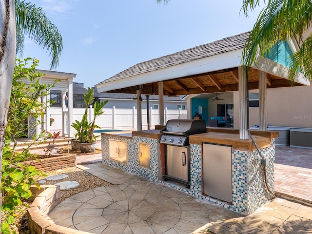 view of patio / terrace with area for grilling, a ceiling fan, fence, a gazebo, and an outdoor kitchen