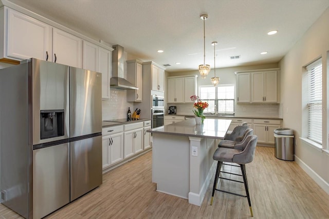 kitchen featuring a kitchen bar, light wood-style flooring, a center island, stainless steel appliances, and wall chimney range hood