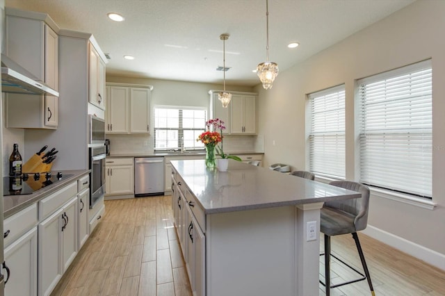 kitchen with appliances with stainless steel finishes, a kitchen breakfast bar, tasteful backsplash, light wood-type flooring, and a center island