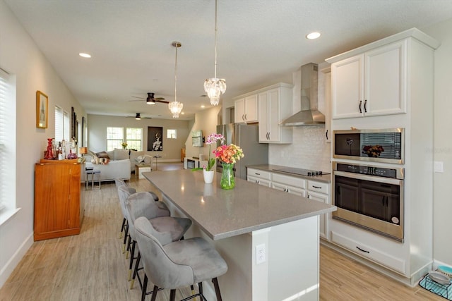 kitchen with a breakfast bar, a center island, white cabinetry, stainless steel appliances, and wall chimney exhaust hood