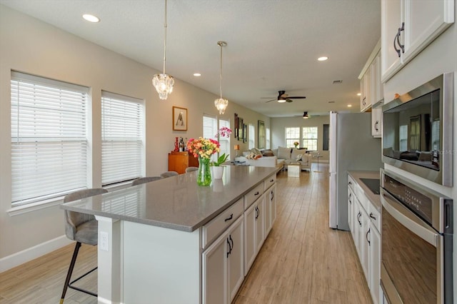 kitchen with a kitchen bar, a kitchen island, stainless steel appliances, white cabinets, and light wood finished floors