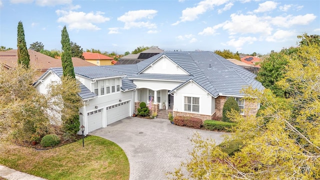 view of front of home with decorative driveway, stone siding, an attached garage, and stucco siding