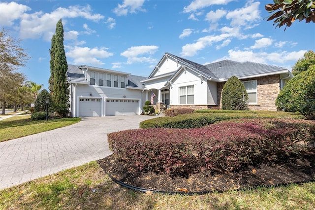 view of front facade with a tile roof, stucco siding, decorative driveway, a garage, and stone siding