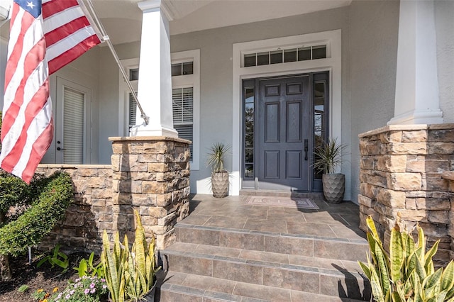 entrance to property with covered porch, stone siding, and stucco siding