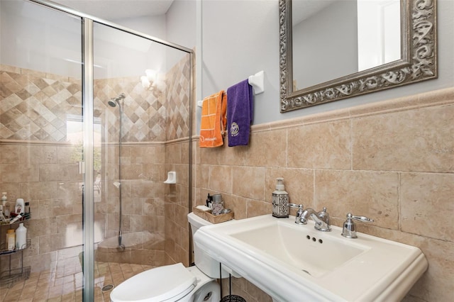 bathroom featuring a wainscoted wall, toilet, a sink, tile walls, and a shower stall