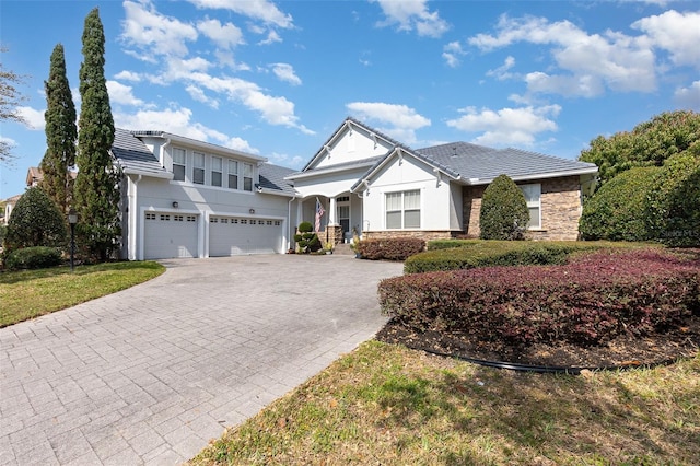 view of front of house with an attached garage, stucco siding, stone siding, a tile roof, and decorative driveway