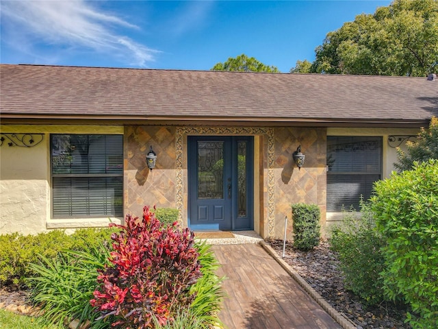 entrance to property with stucco siding and roof with shingles