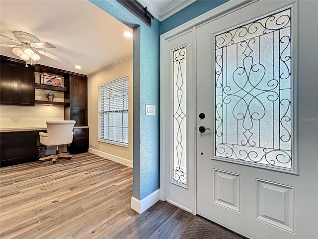 entrance foyer featuring baseboards, light wood-style flooring, built in desk, crown molding, and a textured wall