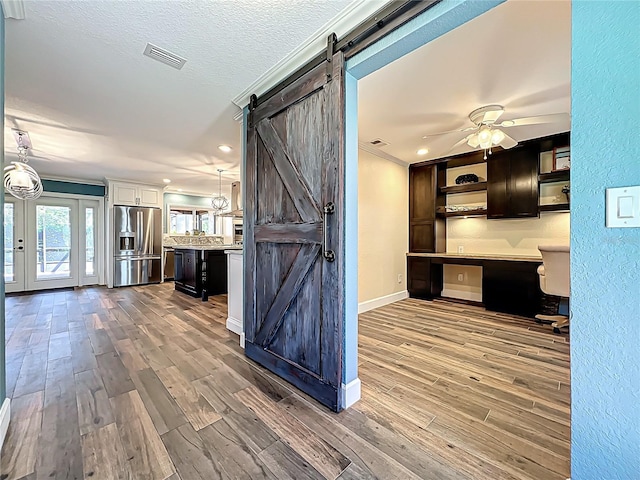 kitchen with visible vents, wood finished floors, built in desk, a barn door, and stainless steel fridge