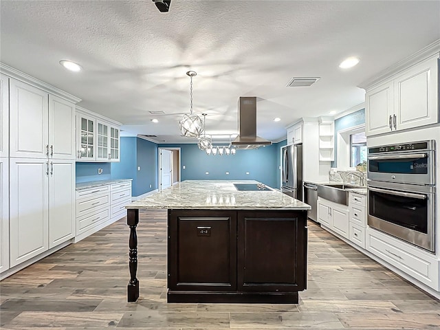 kitchen featuring visible vents, a center island, appliances with stainless steel finishes, white cabinets, and island range hood