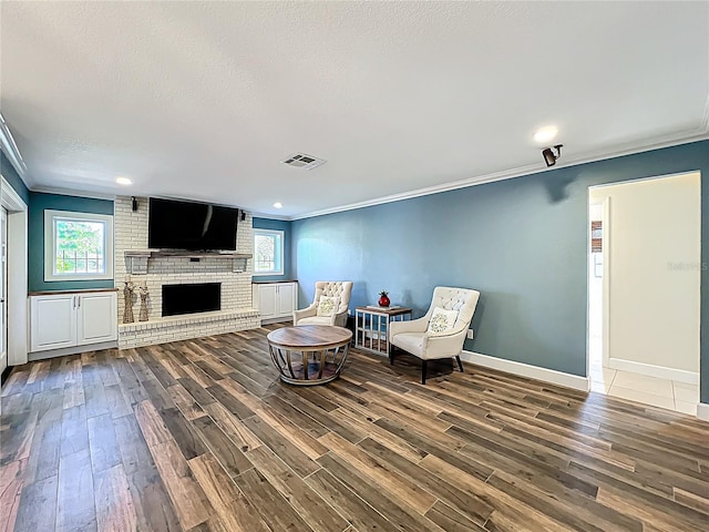 sitting room with wood finished floors, visible vents, plenty of natural light, a fireplace, and crown molding