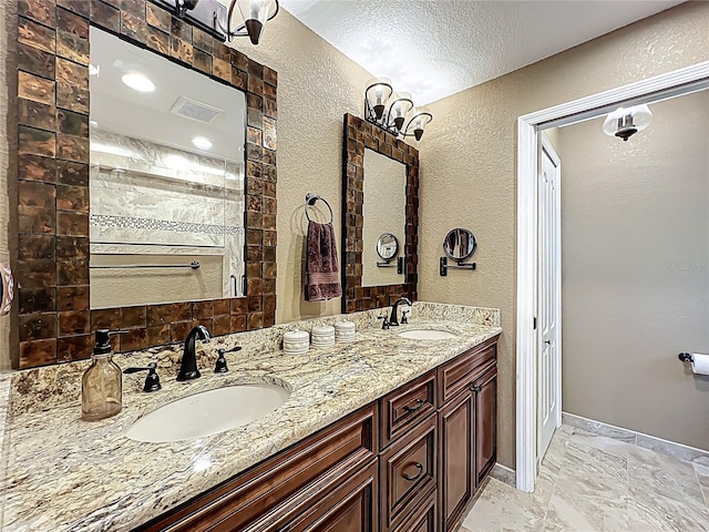 full bath with double vanity, a textured wall, visible vents, and a sink