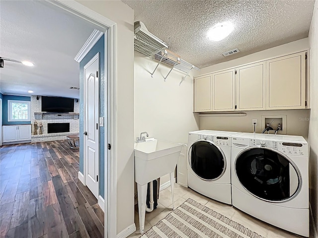 laundry room with washer and clothes dryer, visible vents, cabinet space, and a textured ceiling