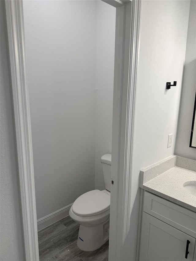 bathroom with vanity, toilet, wood finished floors, and baseboards