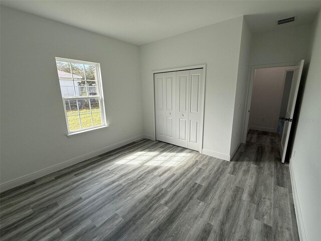 unfurnished bedroom featuring wood finished floors, visible vents, a closet, and baseboards