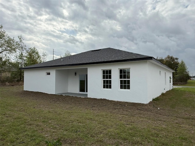 rear view of property featuring a yard, roof with shingles, and stucco siding