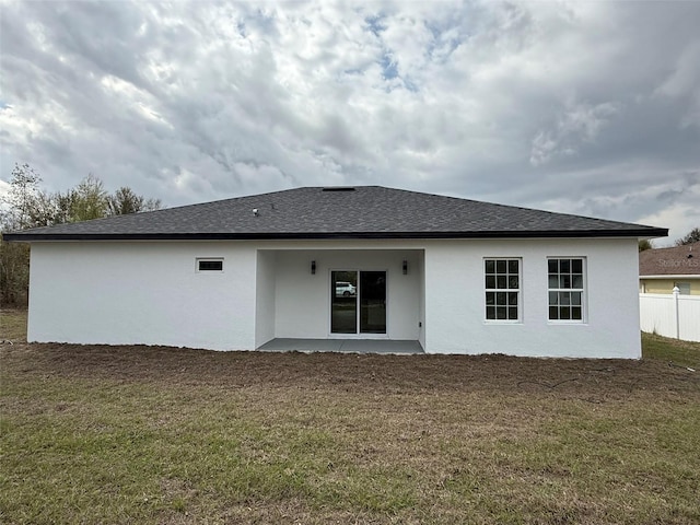 back of house featuring a lawn, a shingled roof, fence, and stucco siding