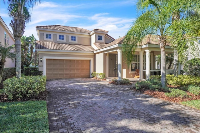 mediterranean / spanish house with a tile roof, covered porch, stucco siding, decorative driveway, and a garage