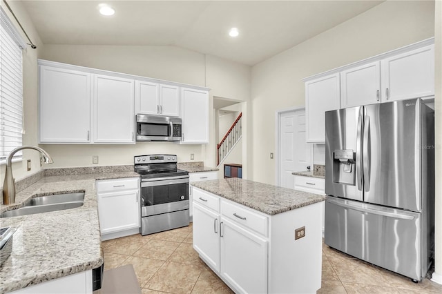 kitchen featuring a kitchen island, a sink, vaulted ceiling, appliances with stainless steel finishes, and white cabinetry