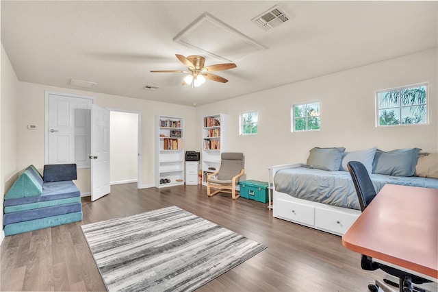 bedroom with attic access, wood finished floors, visible vents, and ceiling fan