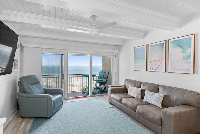 living area featuring a water view, beamed ceiling, ornamental molding, wood finished floors, and a ceiling fan