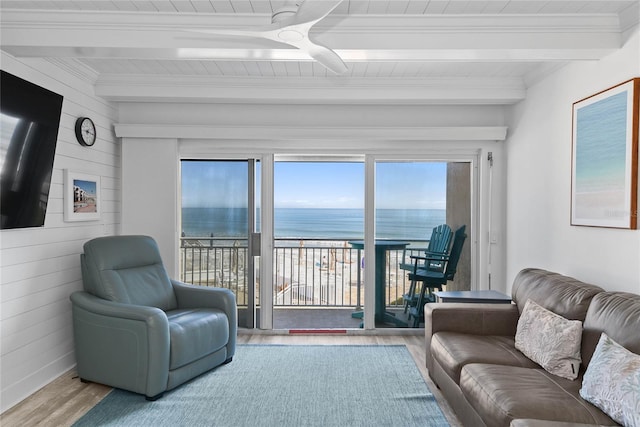 living area with beamed ceiling, a water view, wood finished floors, wood walls, and crown molding