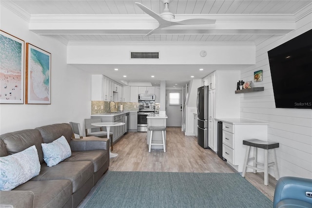 living area with visible vents, light wood-style flooring, wood walls, crown molding, and beamed ceiling