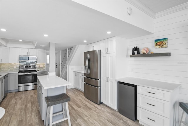 kitchen with ornamental molding, a center island, stainless steel appliances, light wood finished floors, and light countertops