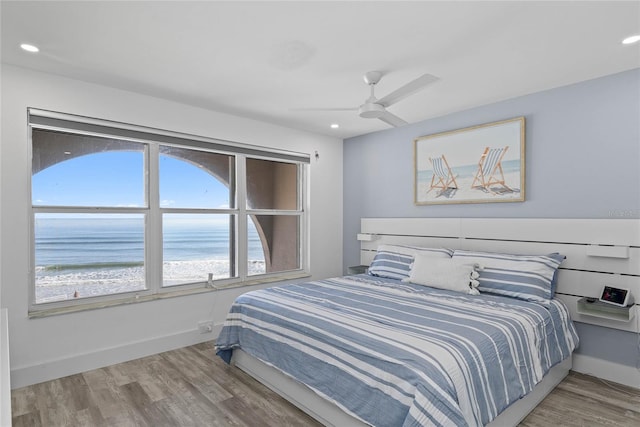 bedroom with wood finished floors, baseboards, recessed lighting, ceiling fan, and a water view