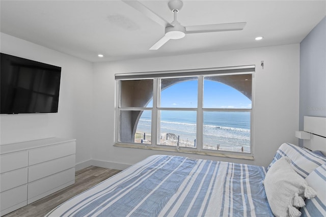 unfurnished bedroom with a water view, a ceiling fan, wood finished floors, recessed lighting, and baseboards