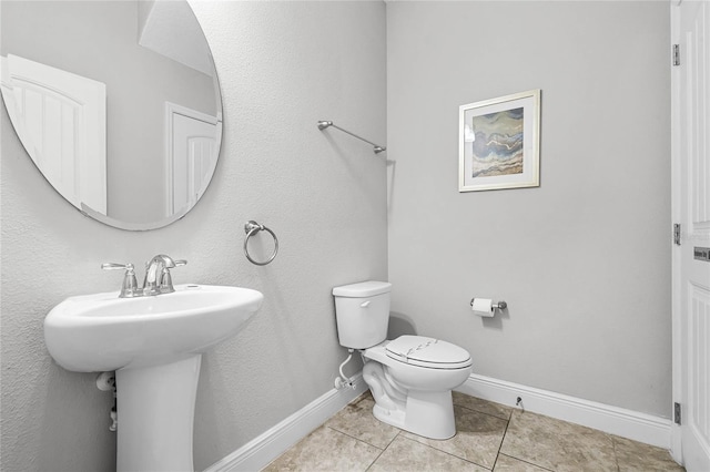 half bath featuring tile patterned floors, baseboards, toilet, and a sink