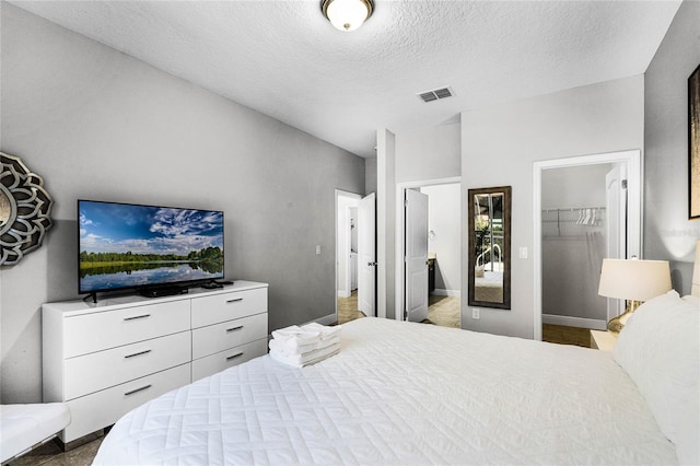 bedroom with visible vents, a spacious closet, a closet, ensuite bathroom, and a textured ceiling