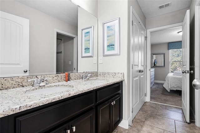 ensuite bathroom with double vanity, visible vents, a textured ceiling, and a sink