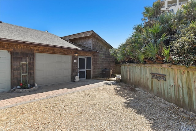 view of home's exterior with fence, dirt driveway, roof with shingles, central AC, and a garage