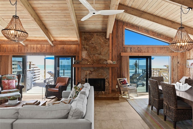 living room featuring lofted ceiling with beams, a healthy amount of sunlight, wood walls, and ceiling fan with notable chandelier