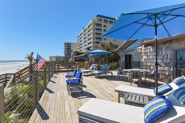 wooden deck with outdoor dining area and a view of the beach