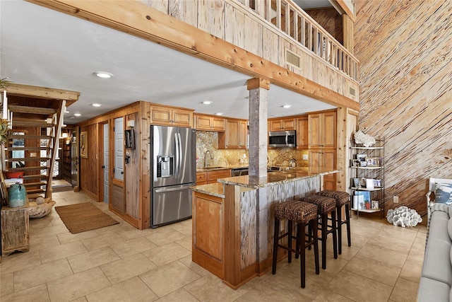 kitchen with visible vents, a sink, stainless steel appliances, wood walls, and stone counters